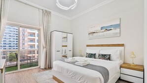 A bedroom with a large bed, a nightstand, a lamp, a mirror, a painting, and a sliding glass door to a balcony. - PVH - 2BR near Marina Promenade (Dubai)