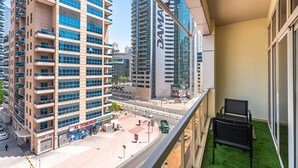 A high-rise building with multiple balconies, a supermarket, and a road with vehicles. - PVH - 2BR near Marina Promenade (Dubai)