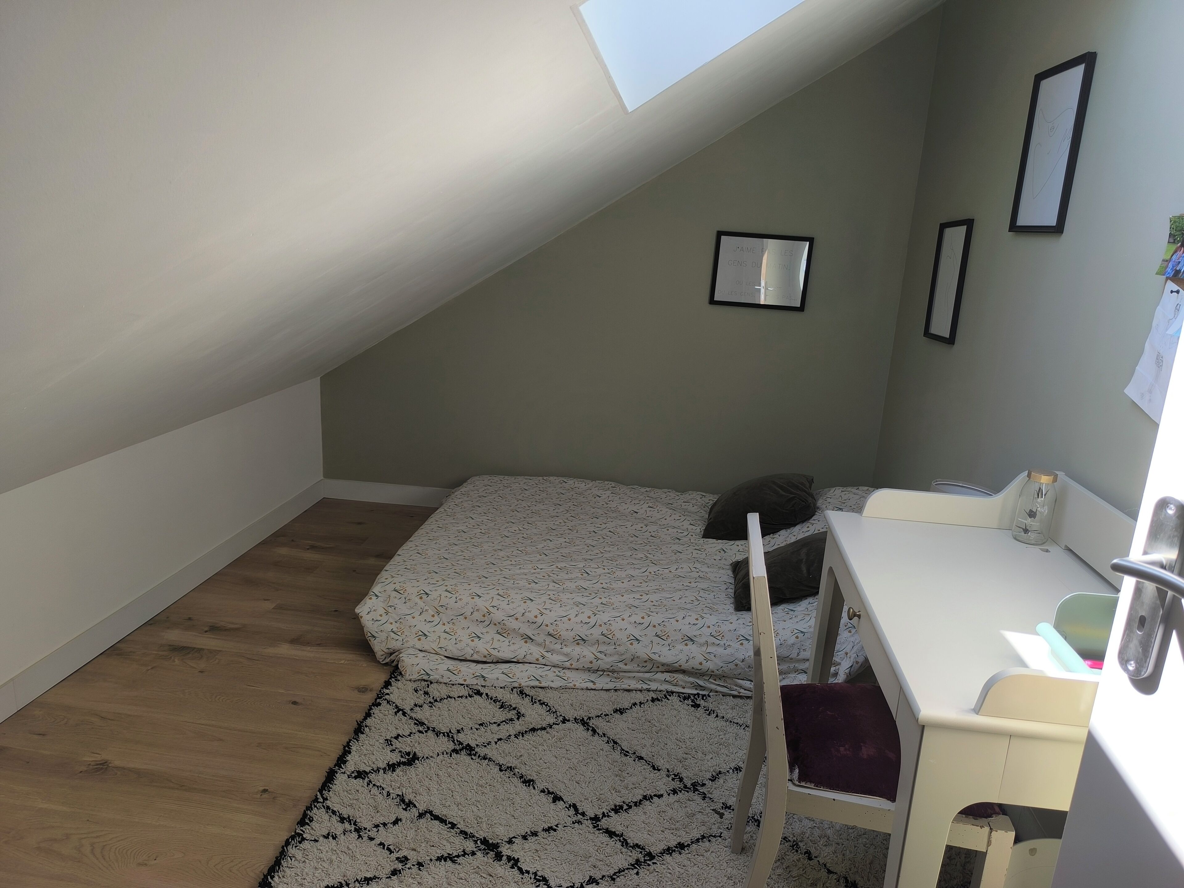 A small, sloped room with a bed, a desk, and a chair.