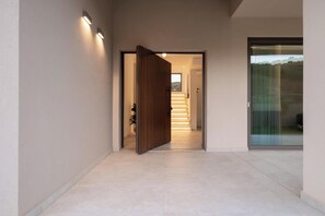 A modern hallway with a wooden door, a staircase, and a glass door leading to a view. - Villa Neratzia - Luxury Escape (Platanias)