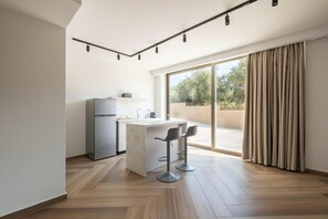 A modern kitchen with a built-in island, bar stools, and a sliding glass door leading to a balcony. - Villa Neratzia - Luxury Escape (Platanias)
