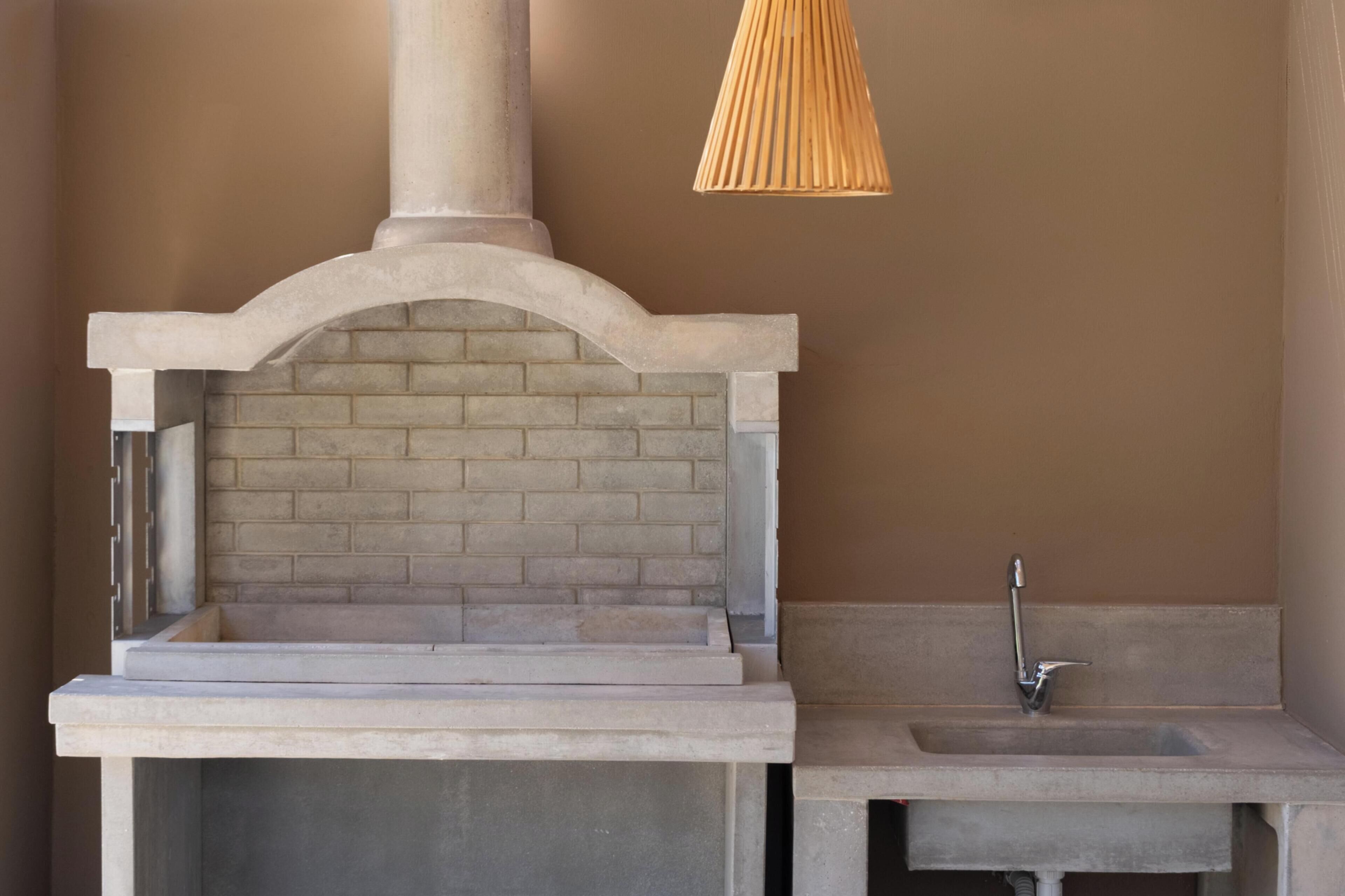 A stone-built outdoor kitchen with a brick oven, a sink, and a hanging light fixture.