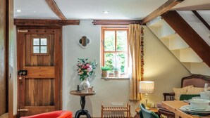 A rustic interior with a wooden door, a small table with a vase, a window with curtains, and a staircase. - Beautiful Two BD Cottage in Oxfordshire (Warborough)