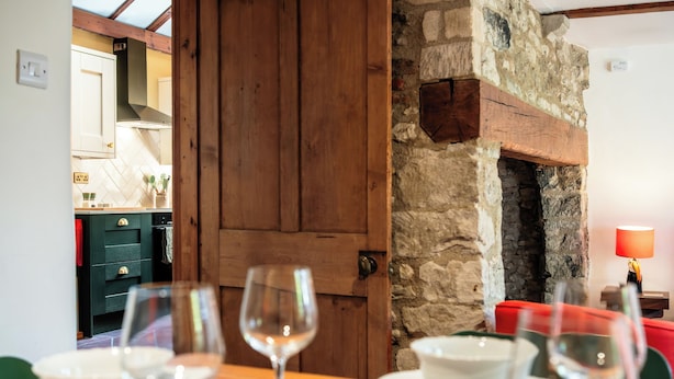 A dining area with a table set for two, a stone wall, and a wooden door. - Beautiful Two BD Cottage in Oxfordshire (Warborough)