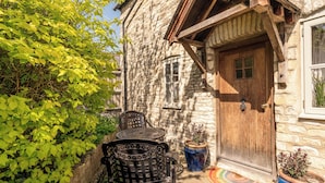 A stone building with a wooden door, a small window, and a doorbell. There are two metal chairs and a potted plant near the door. - Beautiful Two BD Cottage in Oxfordshire (Warborough)