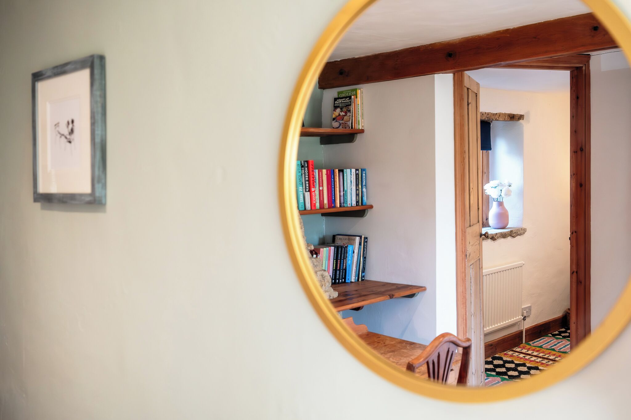 Een ronde spiegel toont een kamer met een boekenkast, een radiator en een vloer met een patroon.
