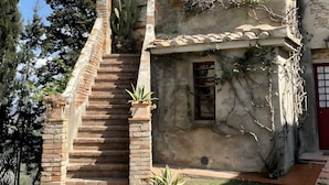 Un bâtiment à deux étages, avec un escalier menant à l’entrée, un petit jardin et un ciel d’un bleu éclatant.