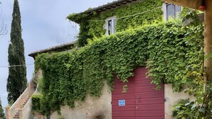 Un bâtiment avec une porte rouge, un patio couvert et un escalier en pierre menant à l’entrée.