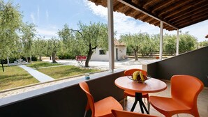 Un'area salotto esterna coperta con sedie arancioni e un tavolo, affacciata su un giardino con alberi e un'auto rossa.