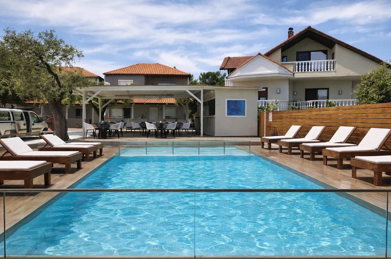 A swimming pool with lounge chairs, a covered seating area, and a building with a tiled roof.