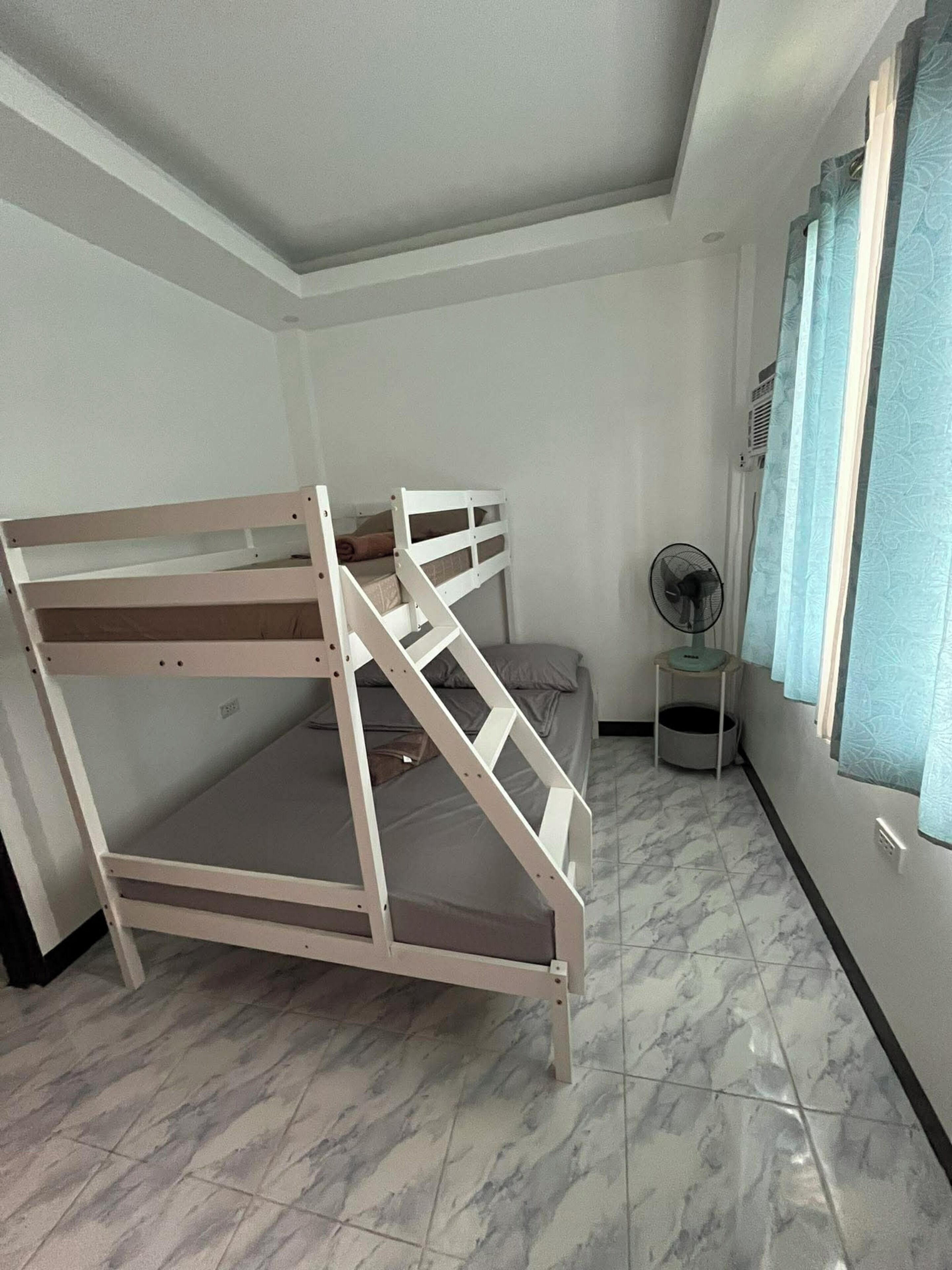 A bunk bed in a room with a fan and a window with curtains.