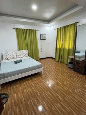 A room with a bed, a desk, a chair, a small cabinet, and a ceiling fan.