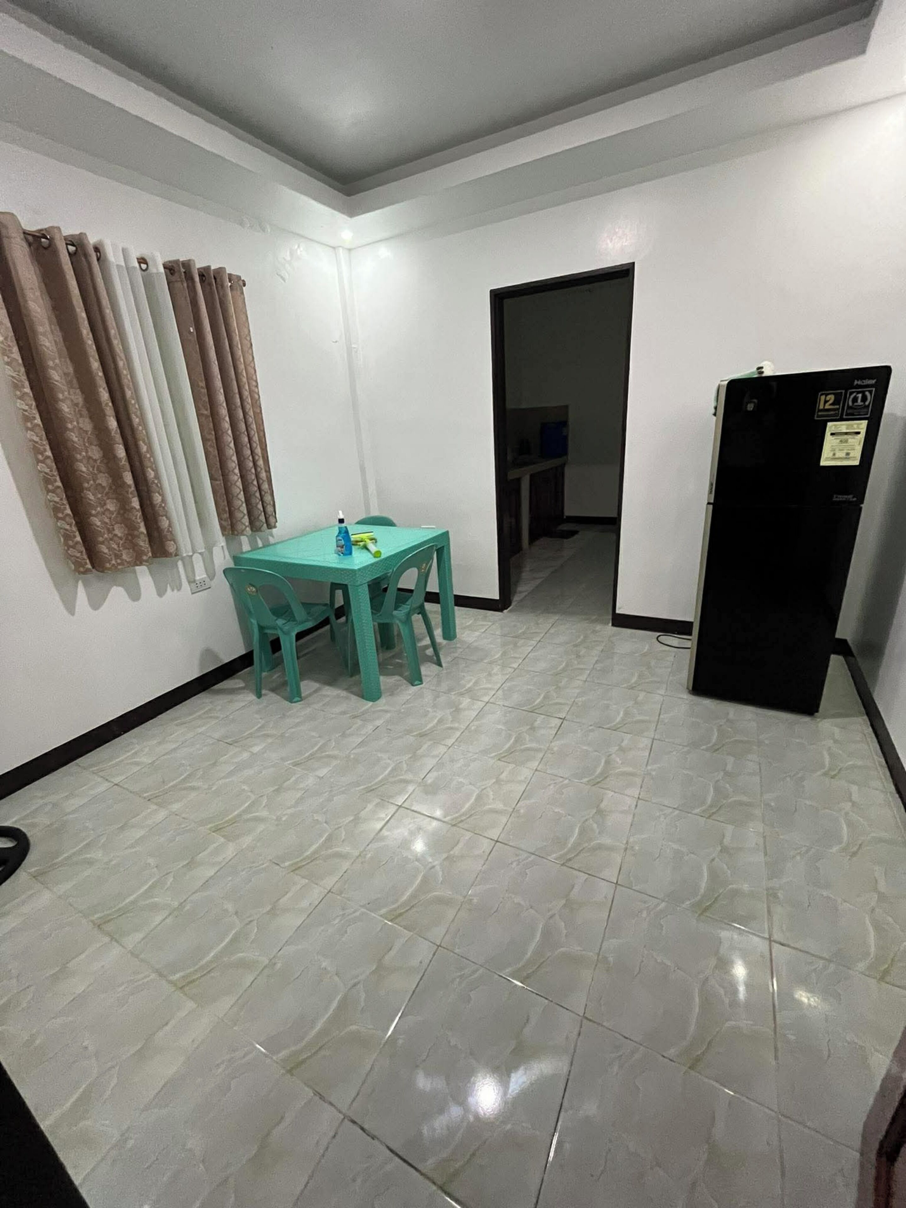 A small, clean room with a tiled floor, a table with chairs, a refrigerator, and a door leading to another room.