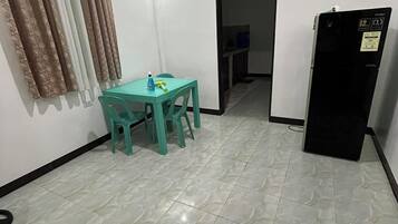 A small, clean room with a tiled floor, a table with chairs, a refrigerator, and a door leading to another room.