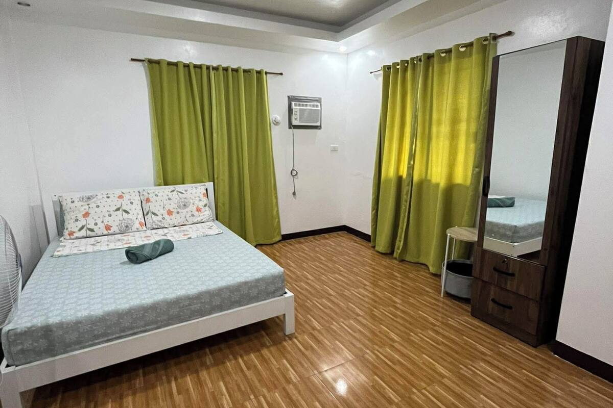 A bedroom with a bed, a fan, a small cabinet, and a mirror.