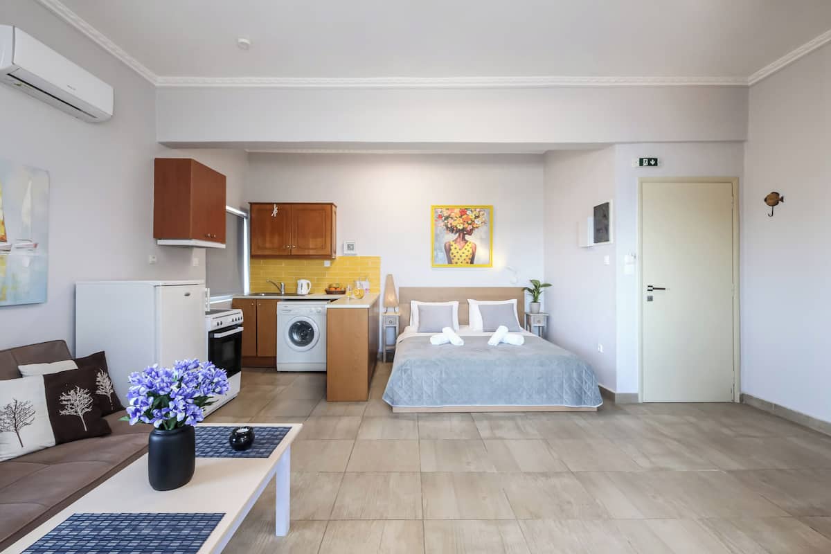 Habitación de hotel pequeña con kitchenette, una cama, un sofá y una mesita con un jarrón de flores.
