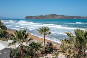 A beach view with palm trees, a sandy shore, and a distant mountain. - Nefeli Seafront Studios (Chania)
