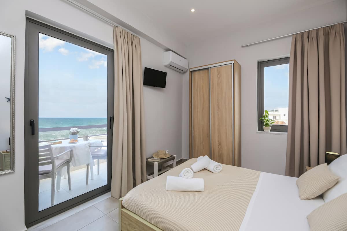 Habitación de hotel con balcón, cama con toallas, televisor y ventana con cortinas.