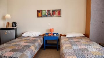 A room with two beds, a small table with a lamp, a refrigerator, and a wall-mounted artwork.