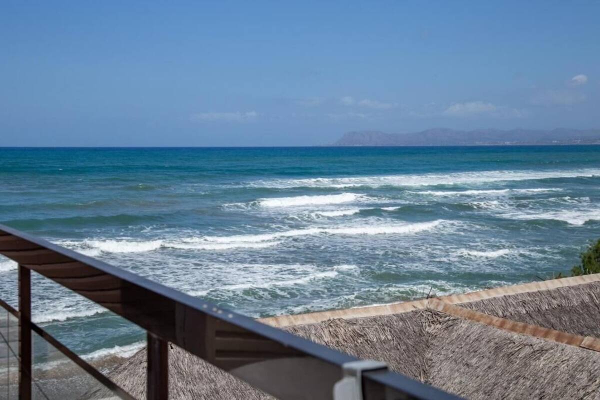 Vista costera con olas, barandilla de madera y montañas distantes.