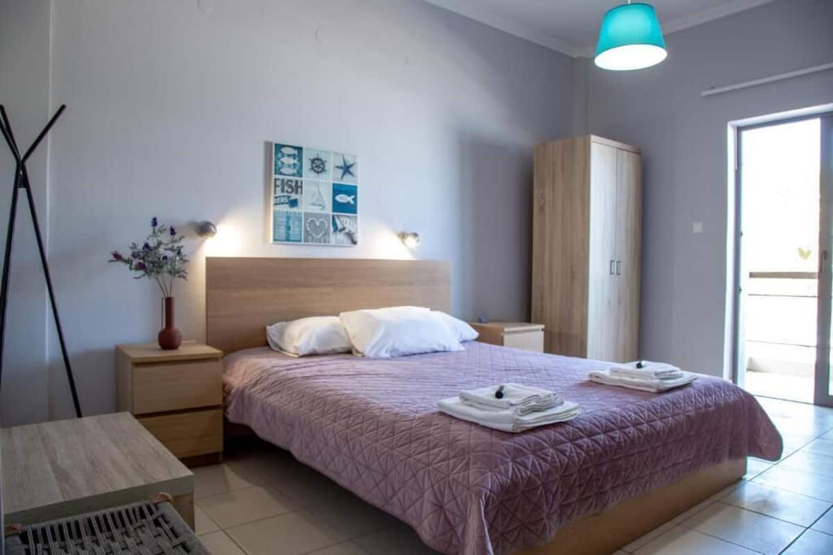 Un dormitorio con cama, mesitas de noche, armario de madera, una obra de arte en la pared y una lámpara colgante.
