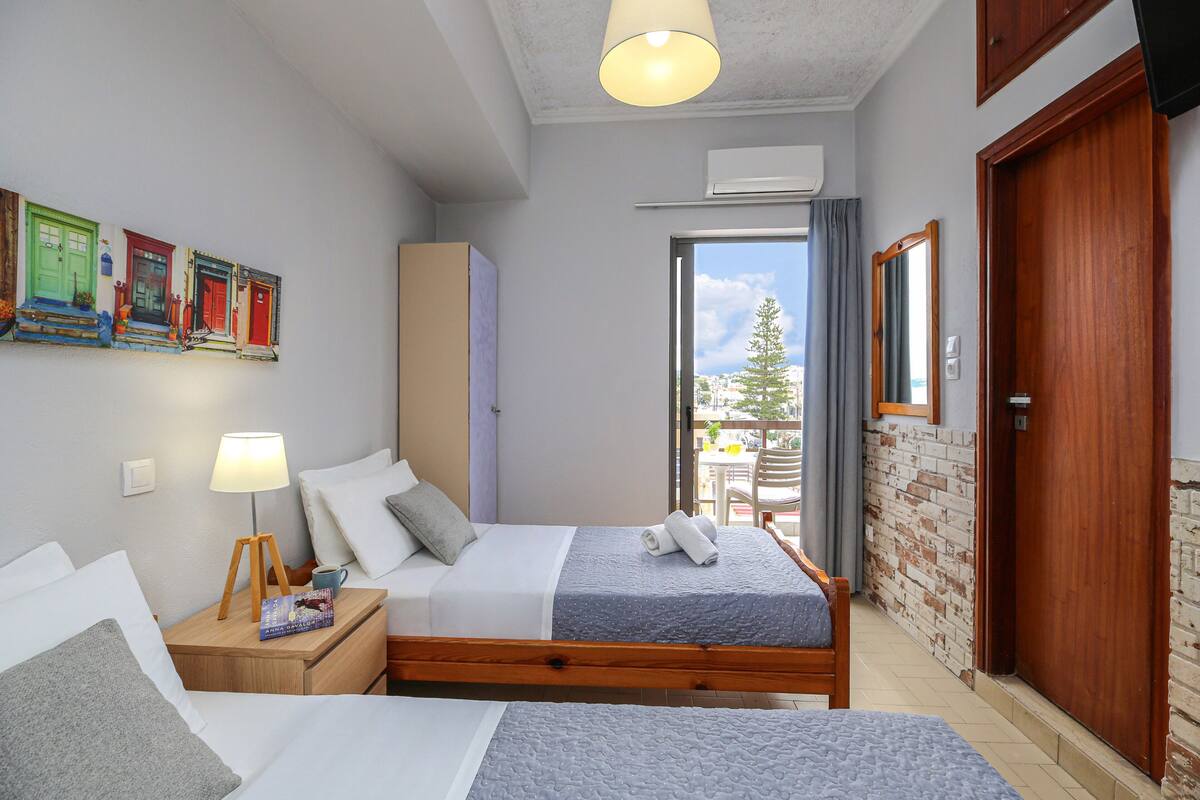 Un dormitorio con cama, mesita de noche, lámpara y vistas al exterior.