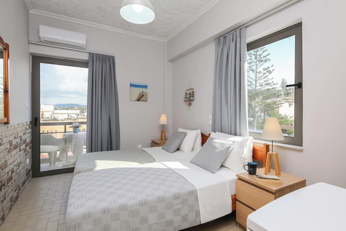 Habitación de hotel con cama, mesita de noche, lámpara y vistas al exterior.