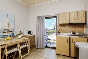 A kitchen with wooden cabinets, a microwave, a sink, and a view of the outside. - Nefeli Seafront Studios (Chania)