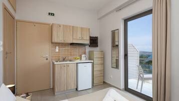 A compact hotel room with a kitchenette, a balcony with a chair, and a view of the outdoors.