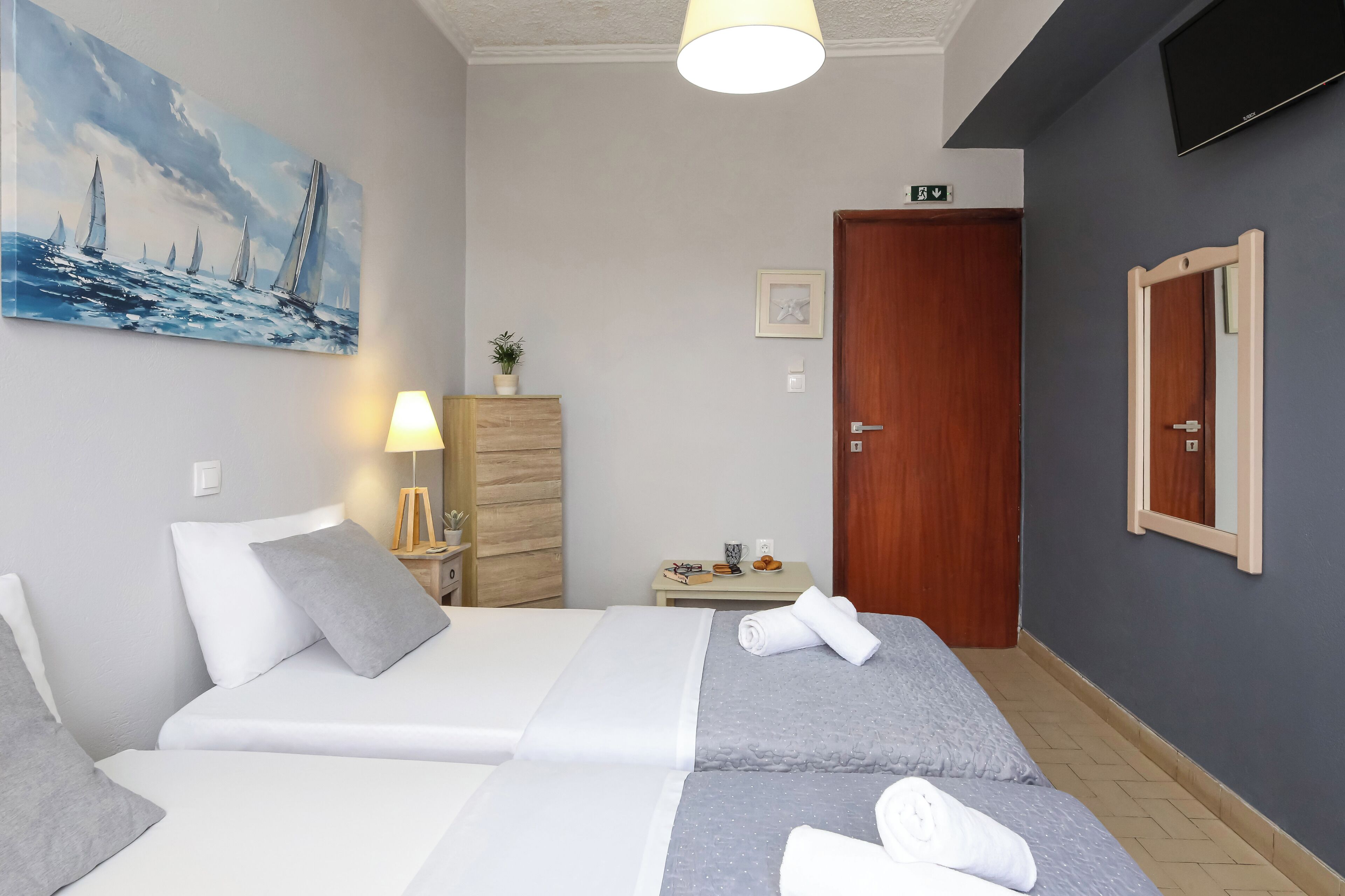 Et hotelværelse med en seng, et maleri, en lampe, et lille bord med en plante og et fjernsyn ophængt på væggen.