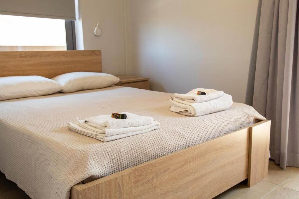 A neatly made bed with a wooden headboard, a bedside table, and a window with curtains.