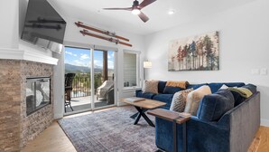 A living room with a fireplace, a blue sofa, a wooden coffee table, and a ceiling fan. - Luxury Keystone Condo - Lodge & Spa Access & 5 Min Drive to Slopes! (Keystone)