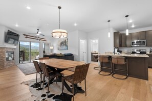 A modern kitchen with a central island, bar stools, and a dining area with a wooden table and chairs. - Luxury Keystone Condo - Lodge & Spa Access & 5 Min Drive to Slopes! (Keystone)