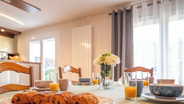 En frukostuppdukning med croissanter, en vas med blommor och ett bord med koppar och ett glas apelsinjuice.
