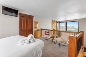 Une chambre d’hôtel avec un lit, une télévision, une porte en bois, une commode, une chaise et un balcon avec vue.