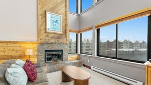 Una sala de estar con chimenea de piedra, un ventanal con vistas a edificios, un sofá con cojines y una mesa de centro de madera.