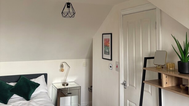 Une chambre à coucher comprenant un lit, une table de chevet, une lampe et une porte donnant sur une autre pièce.