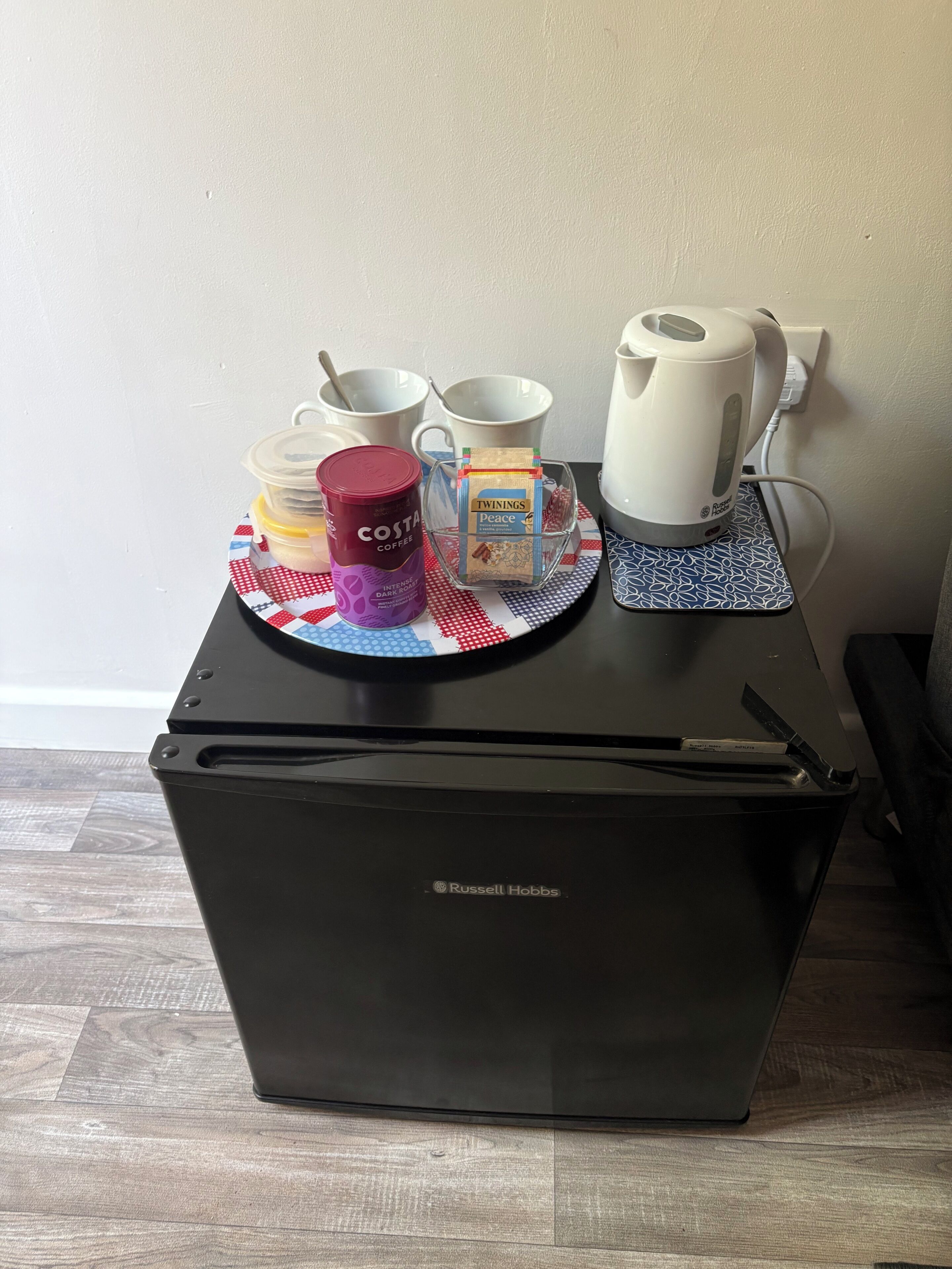 A kitchenette with a coffee maker, a canister, and a box of Twinings tea on a black countertop.