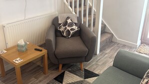 Un salon comprenant un canapé, une petite table avec un mouchoir et une télécommande, un téléviseur fixé au mur et un escalier.