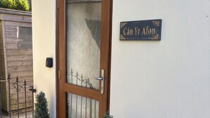 Une porte en bois avec un panneau de verre, une plaque portant l’inscription « Căn Yr Afon », et deux plantes en pot placées de chaque côté de la porte.