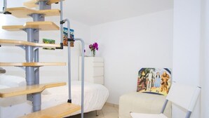Une pièce avec un escalier en colimaçon, un lit, une chaise et un tableau accroché au mur.