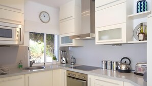 Une cuisine moderne équipée d’un four, d’un micro-ondes et d’un évier intégrés. Il y a une horloge au mur et une fenêtre qui laisse entrer la lumière naturelle.