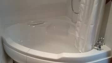 A bathtub with a shower head, a visible drain, and a faucet.