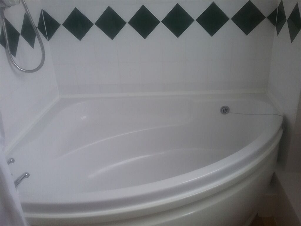 Et hvidt badekar med brusehoved, et hvidt toilet og en væg med diamantmønstret flisebeklædning.