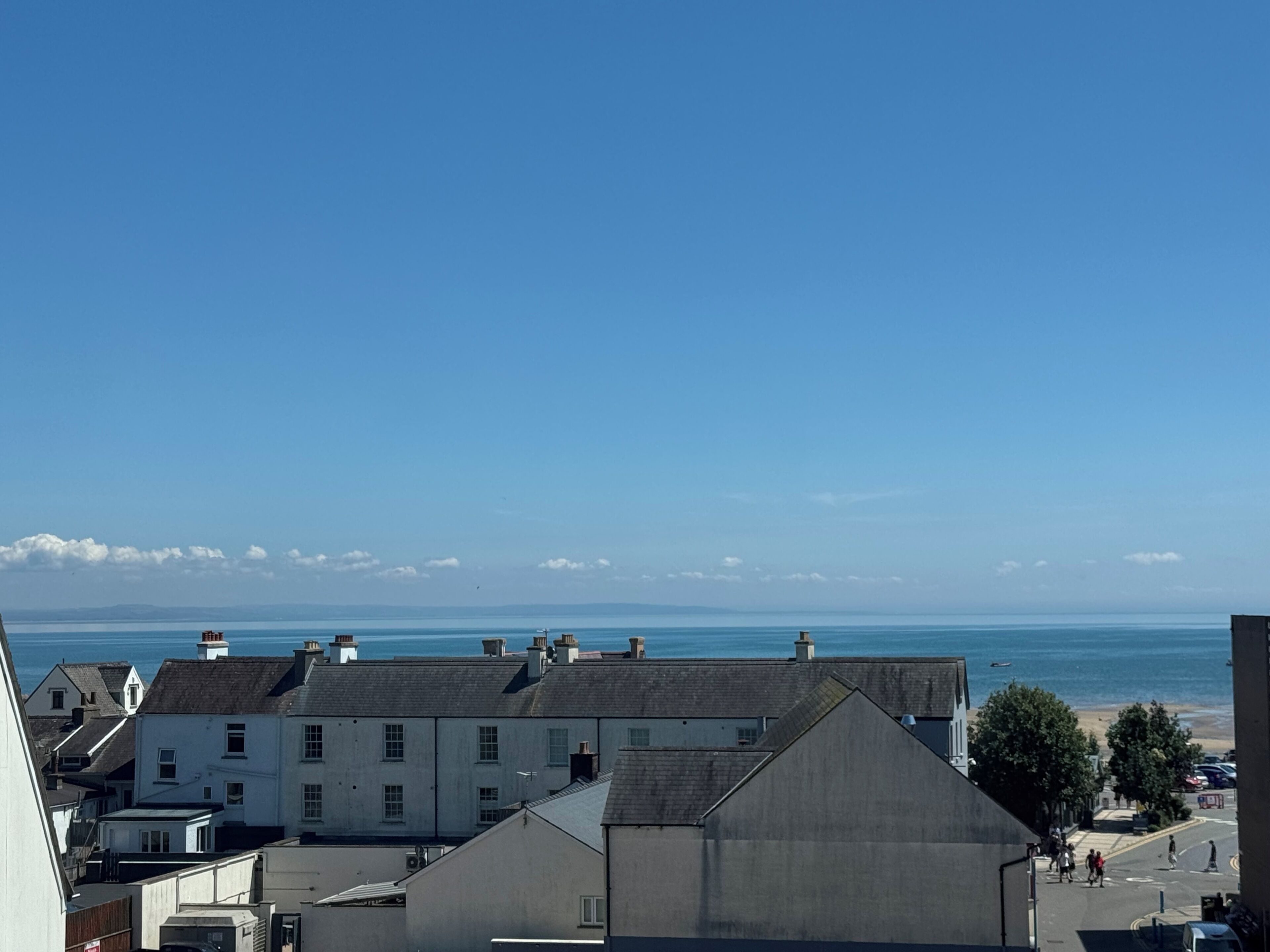 A coastal town with buildings, a clear sky, and the sea in the background.