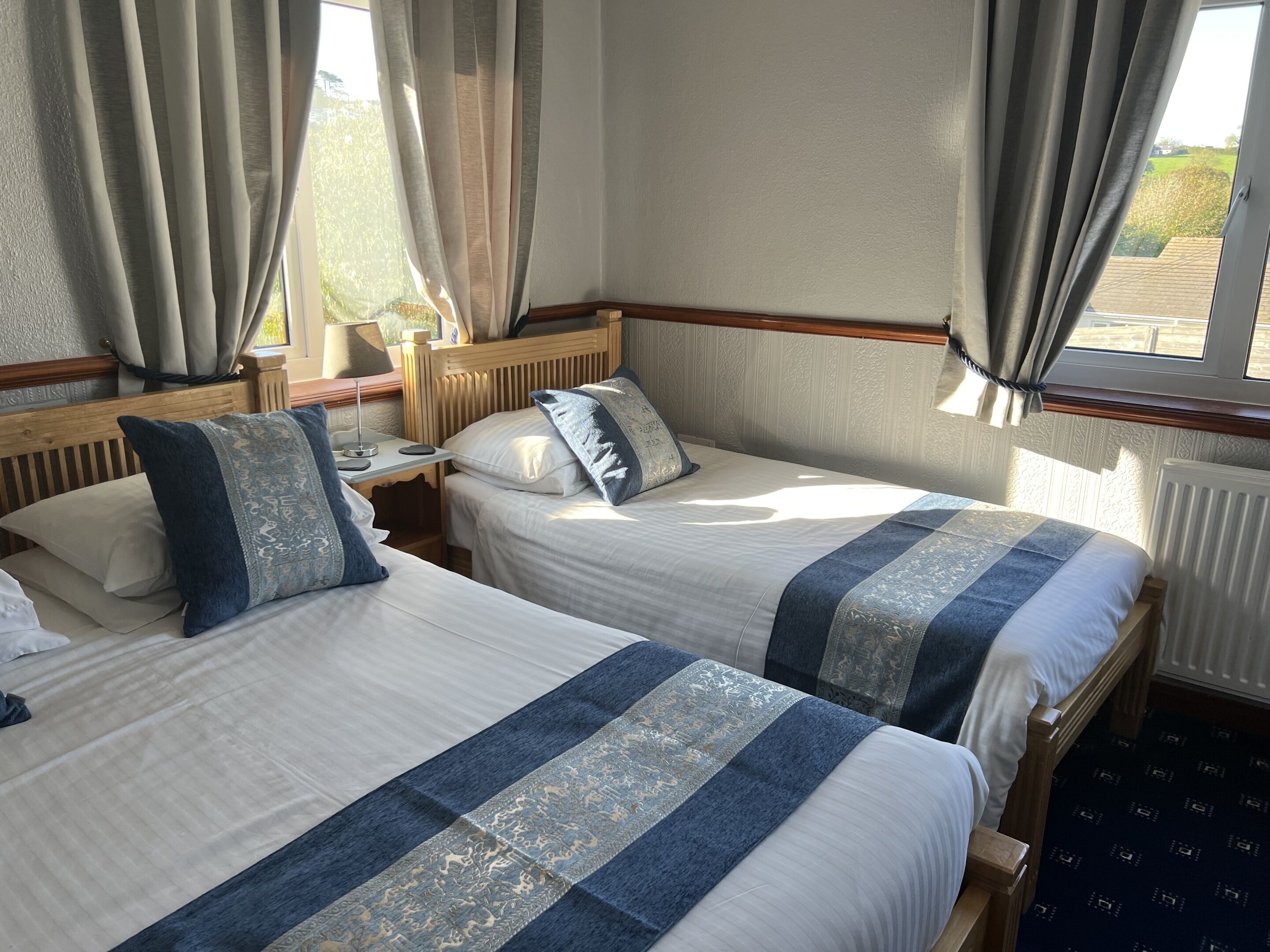A hotel room with two beds, a nightstand, a lamp, and a window with curtains.