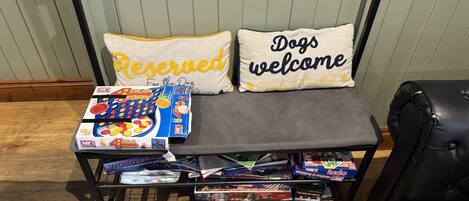 A bench with a 'Reserved' pillow and a 'Dogs welcome' pillow, surrounded by board games and magazines.