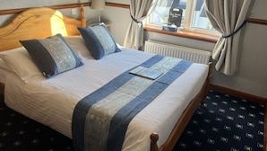 Ein ordentlich bezogenes Bett mit einer blau-weißen Tagesdecke, einem hölzernen Kopfteil und einem Nachttisch mit einer Lampe.