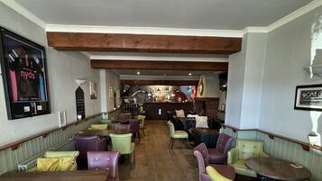 A restaurant with wooden beams, green and purple booths, and a bar in the background.