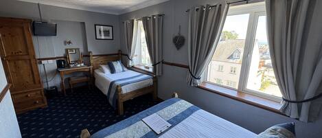 Un dormitorio con cama, escritorio, armario y ventana con cortinas.